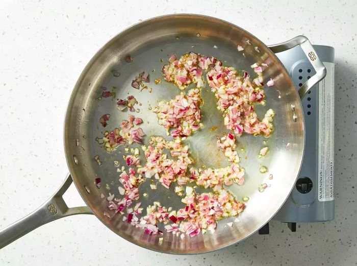 A top-down view of onions and garlic sizzling in a skillet