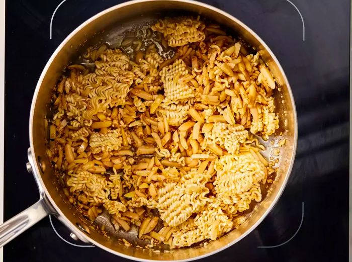 A pan with ramen noodles and sliced almonds roasting to golden perfection.