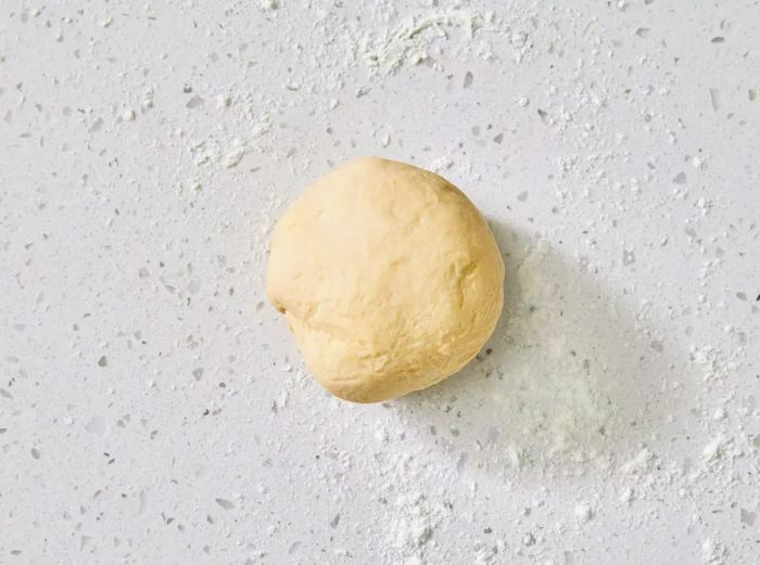 A smooth ball of pasta dough resting on a floured surface