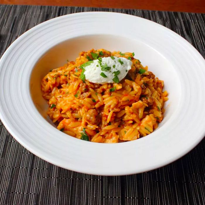 Close-up of a bowl of Chicken and Sausage Orzo, garnished with ricotta cheese and fresh herbs.