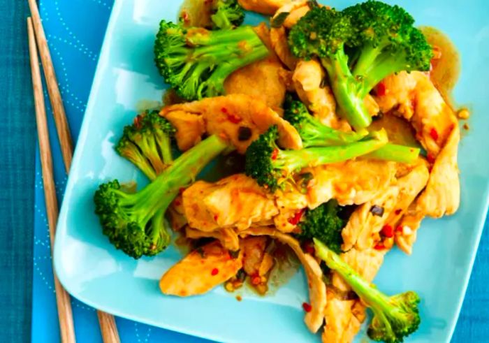 Stir-fried chicken with broccoli served on a plate, accompanied by chopsticks.