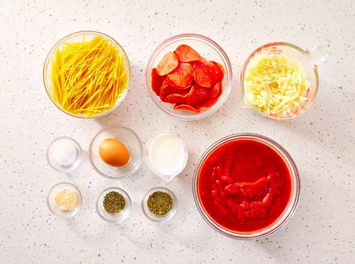 Spaghetti Pizza ingredients arranged in glass bowls on a kitchen counter