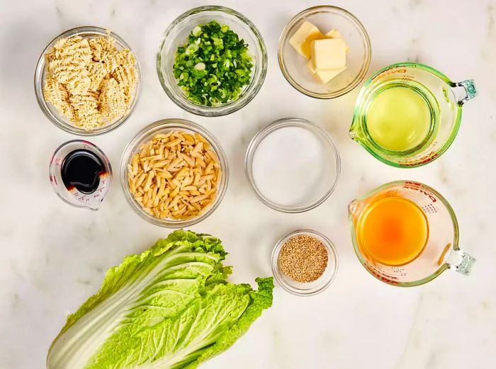 Napa cabbage salad ingredients arranged in glass bowls on a marble countertop.