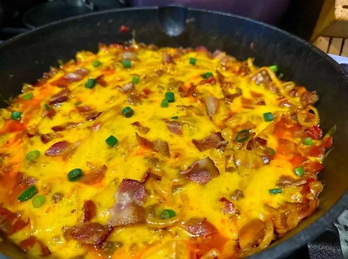 cast iron skillet with spaghetti topped with melted cheese and crispy bacon