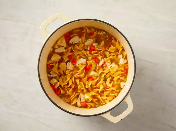 An overhead view of the finished chicken noodle soup simmering in a pot.