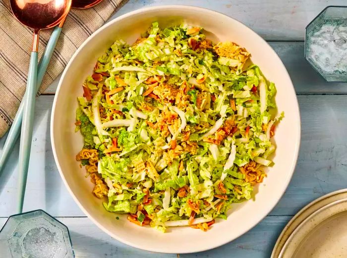 A large bowl of Napa cabbage salad topped with toasted ramen and almonds.