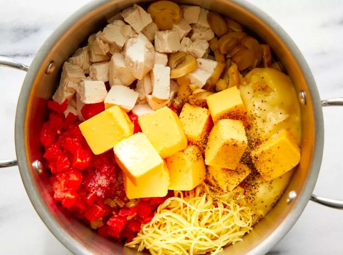 An overhead shot of processed cheese, cream of soup, diced tomatoes, and chopped chicken added to a pot with angel hair pasta.