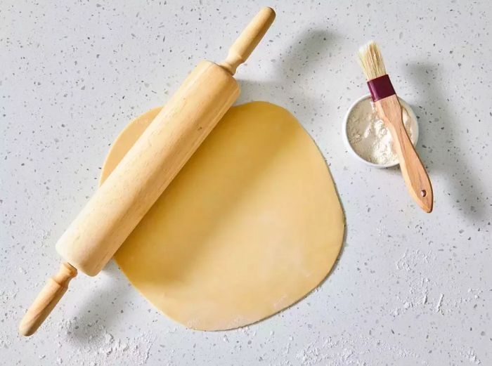 A large sheet of pasta dough rolled out with a rolling pin on a floured surface