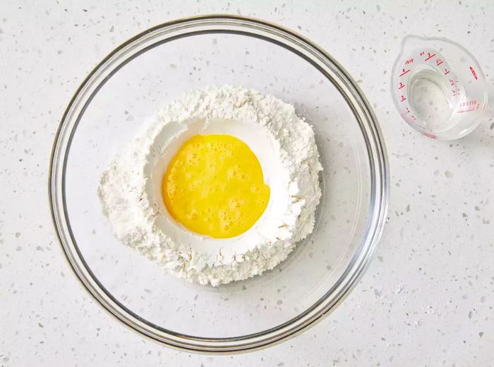 A large glass bowl with a beaten egg surrounded by flour and salt in the center