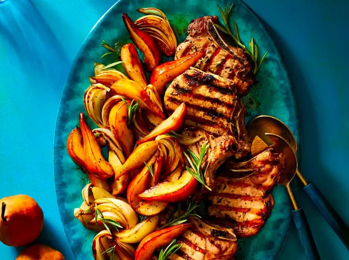 A top-down shot of grilled pork chops paired with pear wedges on a vibrant turquoise platter