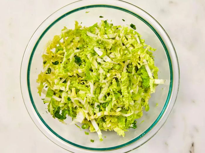 A glass bowl filled with shredded Napa cabbage and green onions.