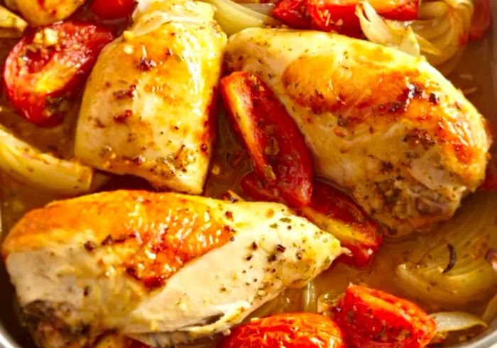 Chicken breasts baked in a dish with tomatoes and onions.