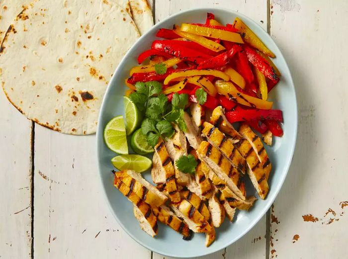 A close-up view of a large plate filled with sizzling grilled chicken fajitas.