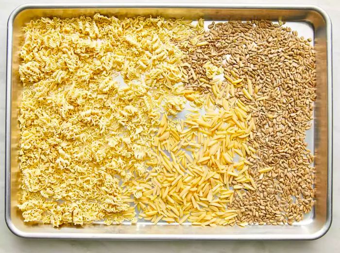 Ramen noodles, seeds, and almonds spread out on a baking tray