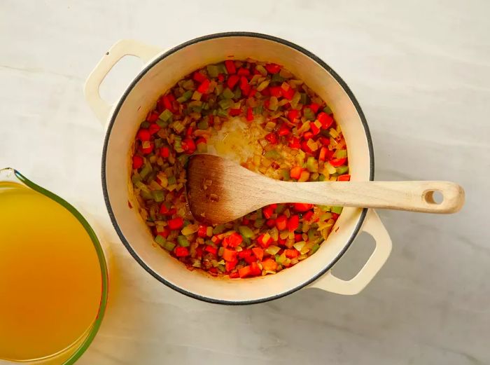 An overhead shot of carrots, onions, celery, thyme, and salt simmering in a pot, with a cup of broth placed nearby.