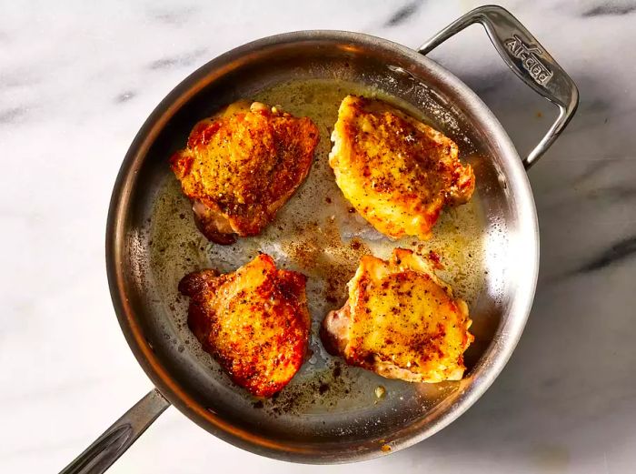 Chicken thighs browning in a skillet.