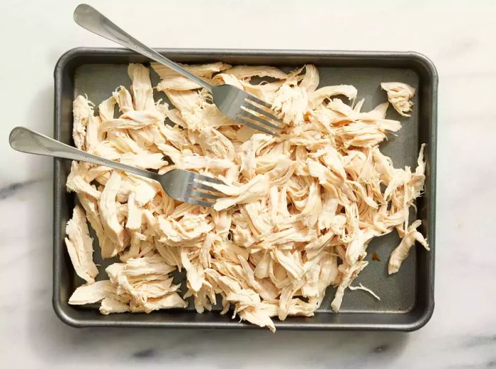 A baking sheet with shredded chicken and two forks