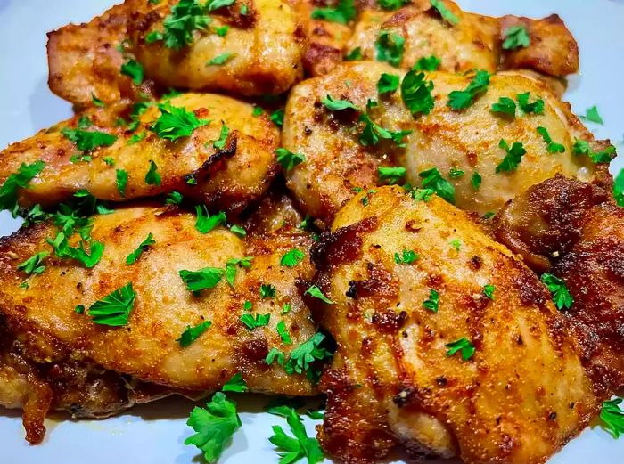 a plate of crispy golden-brown paprika chicken thighs topped with fresh parsley