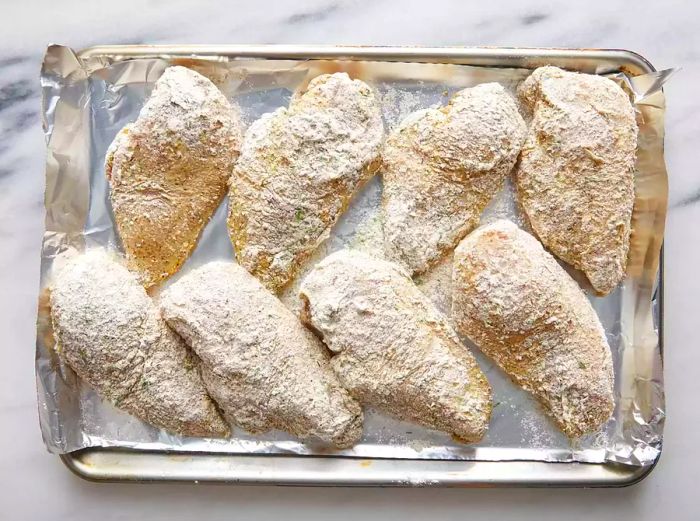 Bird's-eye view of raw, breaded chicken breasts arranged on a tray