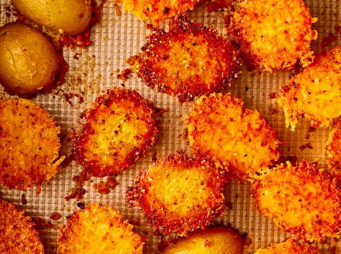 A close-up, overhead view of crispy, golden-brown Parmesan-crusted potatoes on a baking sheet.