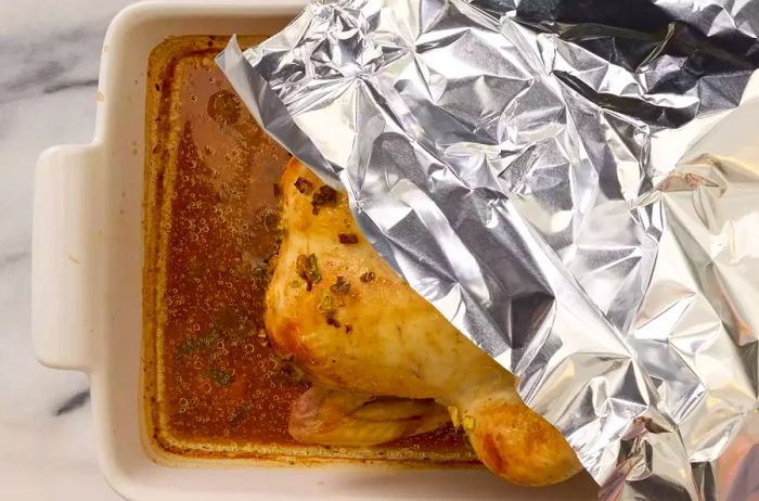 A baking dish with baked beer can chicken, now covered with aluminum foil