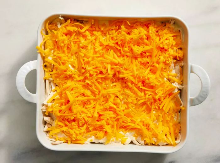 A baking dish with layers of soup mixture, shredded chicken, and melted cheese