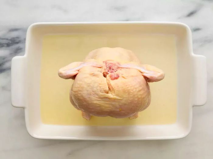 A baking dish with beer at the bottom, and a whole chicken standing upright on a beer can