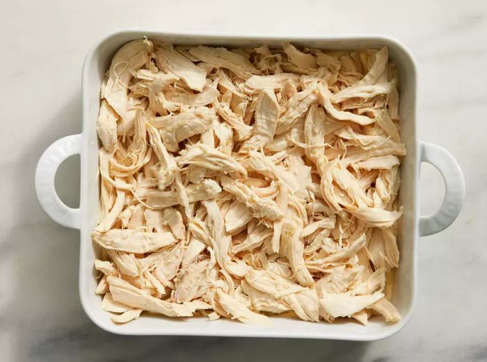 A baking dish with a layer of soup mixture topped with shredded chicken