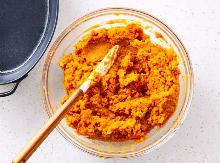 A bowl of mashed sweet potatoes with seasonings placed next to a baking dish