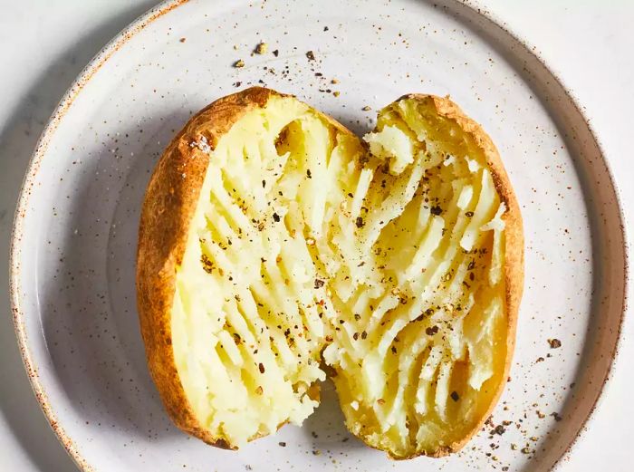 A soft, microwave-baked potato split in half, seasoned with salt and pepper.