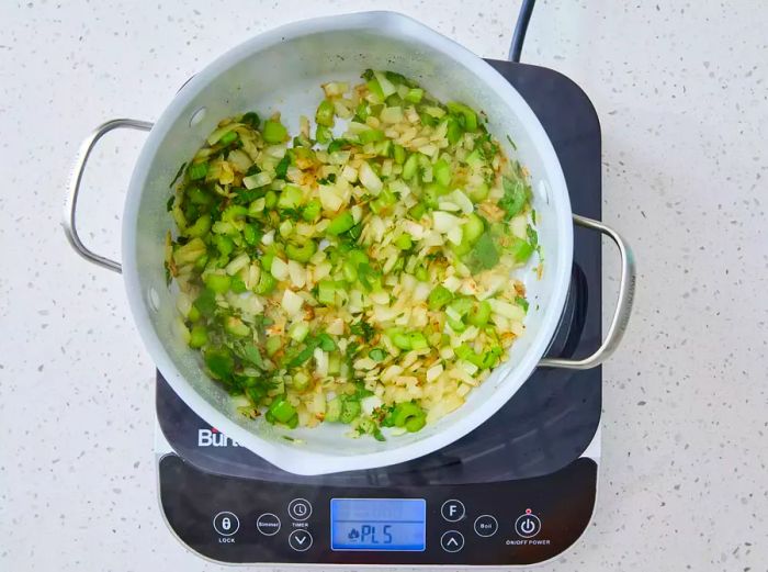 A pot with sautéed onion and celery, seasoned with thyme, sage, salt, and pepper