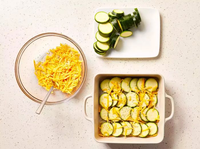 A square baking dish filled with layers of zucchini slices, topped with a cheese and herb mixture.