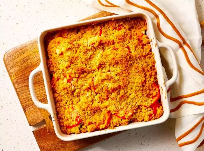 A fully baked tomato and zucchini casserole placed on a wooden cutting board.