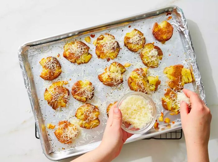 Crispy smashed potatoes being topped with a generous amount of shredded Parmesan cheese.