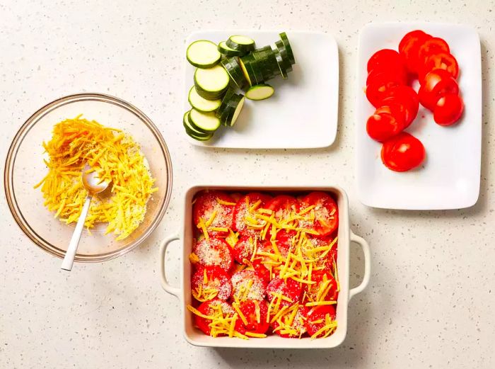 A square baking dish with alternating layers of zucchini slices, cheese, and tomato slices.