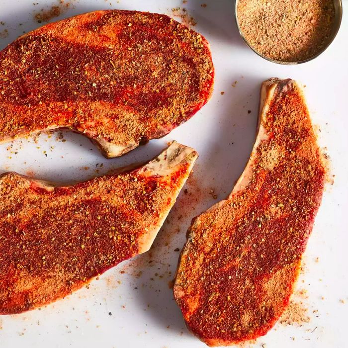 An aerial shot of three raw steaks generously seasoned with a blend of herbs and spices.