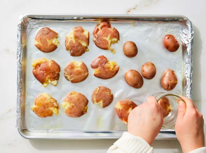 Smashed potatoes being flattened using the bottom of a drinking glass.