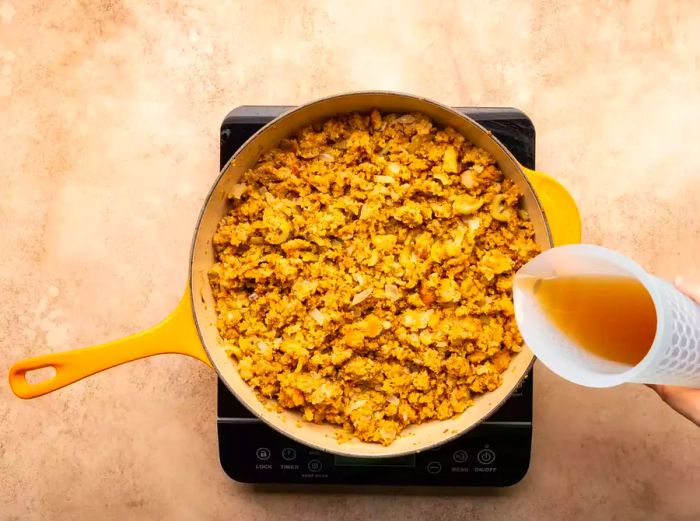 Pouring chicken broth over the stuffing as it cooks in the skillet.