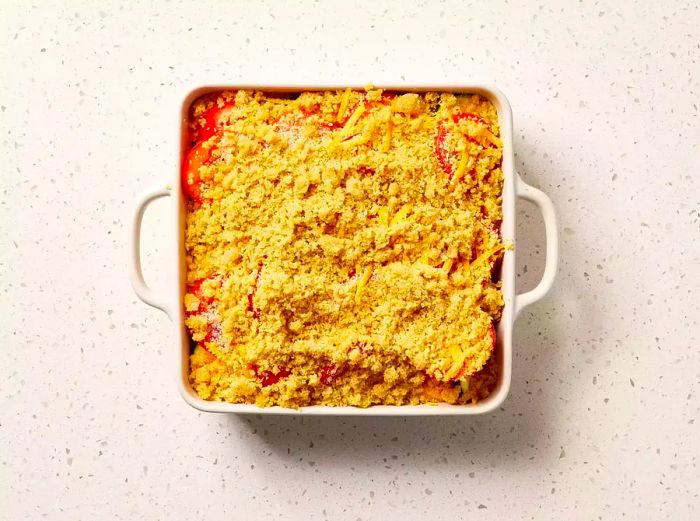 A square baking dish filled with tomato and zucchini casserole, topped with a golden, buttery breadcrumb crust.