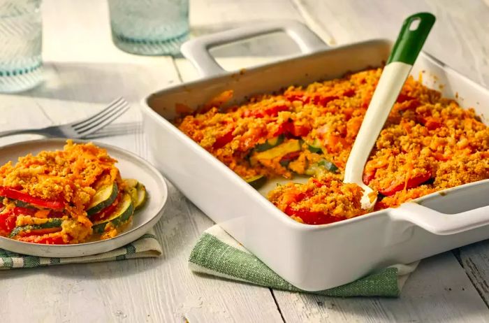 A serving of tomato zucchini casserole topped with crispy, browned breadcrumbs, accompanied by a plated portion.