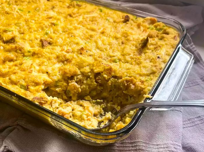 An overhead view of Southern cornbread dressing in a 9x13-inch glass casserole dish with a portion removed, ready to serve.