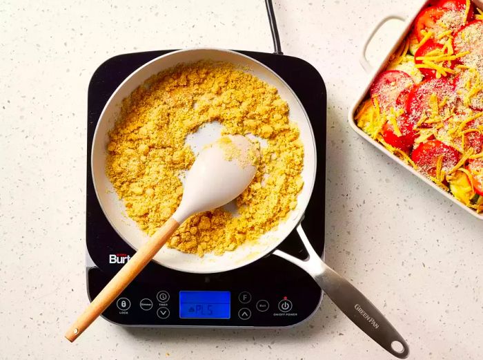 A small skillet with melted butter, onions, and breadcrumbs being stirred with a spoon.