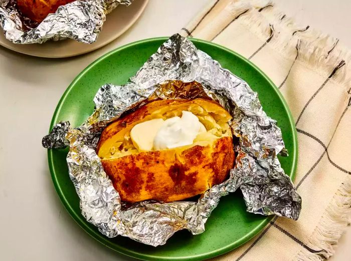 A foil-wrapped slow cooker baked potato served with butter and sour cream.