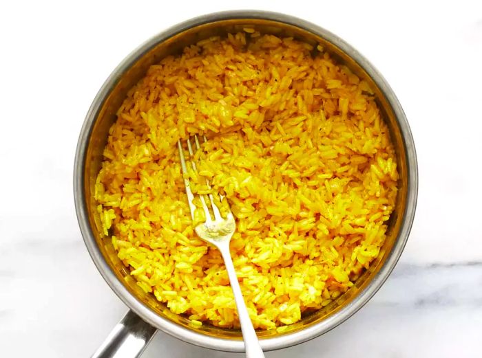 A top-down view of fluffy yellow rice with a fork in a small pot