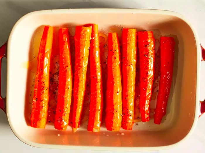 Carrots arranged in a baking dish, coated with olive oil.