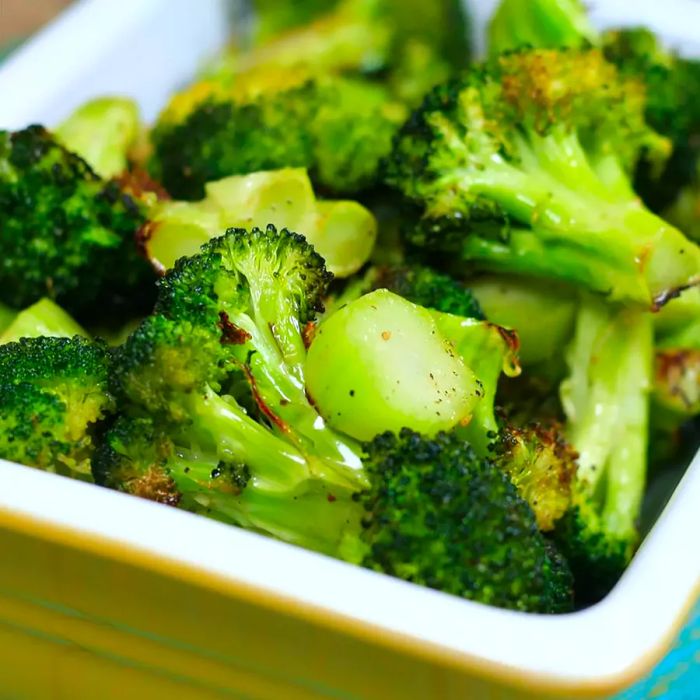 A close-up of perfectly roasted broccoli served in a white bowl