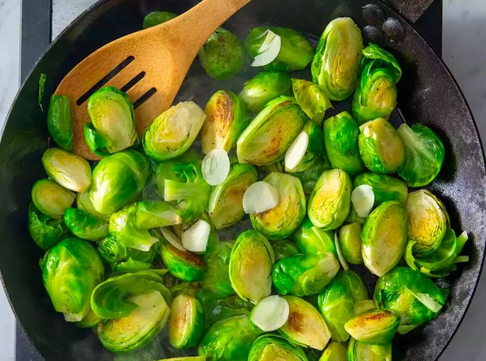 Garlic being added to a skillet of Brussels sprouts.