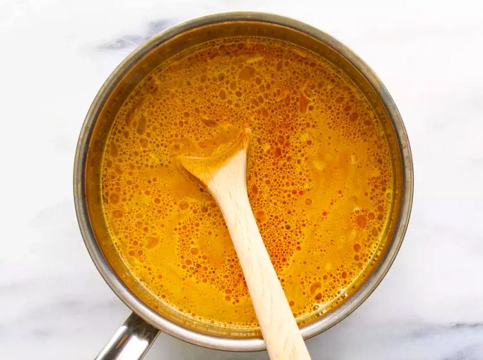 A top-down view of water mixed with ingredients for Cindy's Golden Rice in a small pot, with a wooden spoon