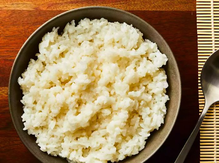 Top-down view of a bowl of sushi rice next to a spoon.