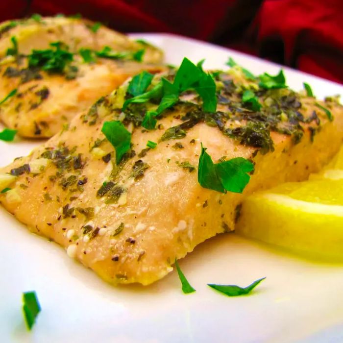 Two perfectly baked salmon fillets topped with freshly chopped parsley and a slice of lemon